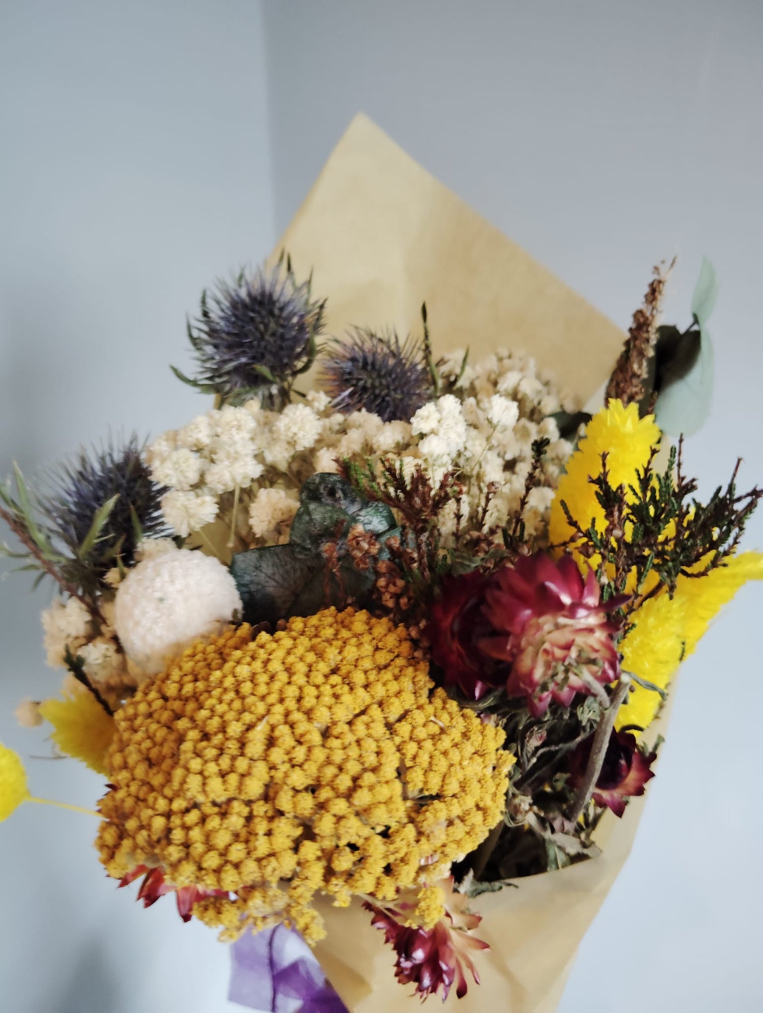 Modern dried flower bunch featuring blue eryngium thistles, bright yellow statice, and white gypsophila.