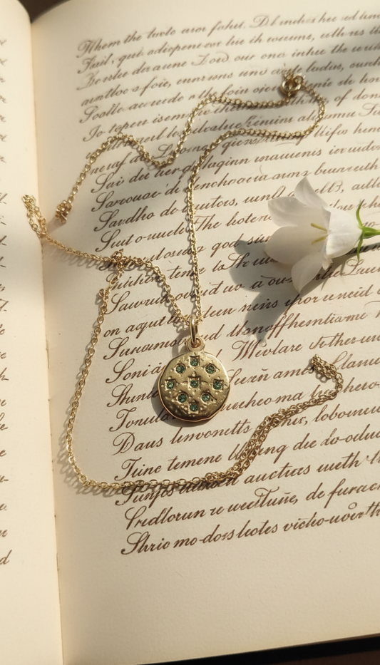 Gold pendant necklace with green crystals on vintage book
