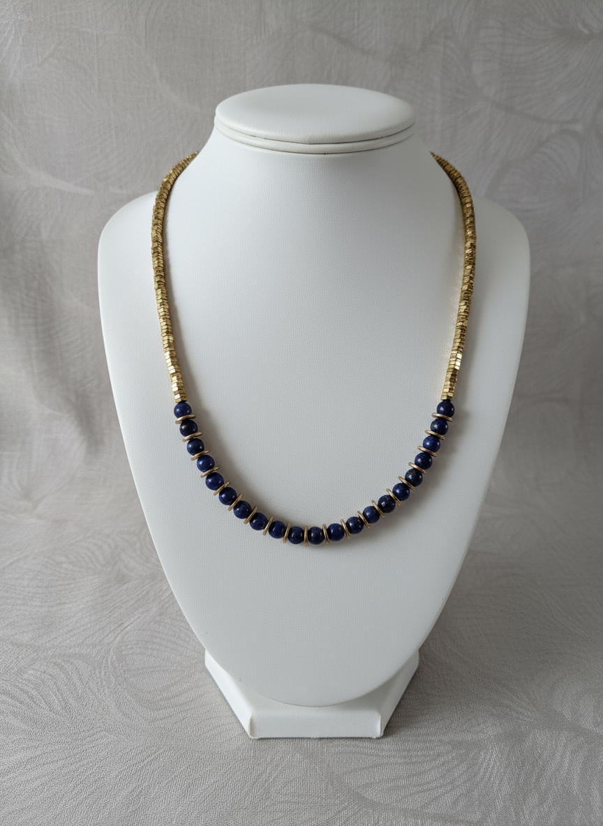 Handcrafted blue lapis lazuli and gold hematite bead necklace on grey background"