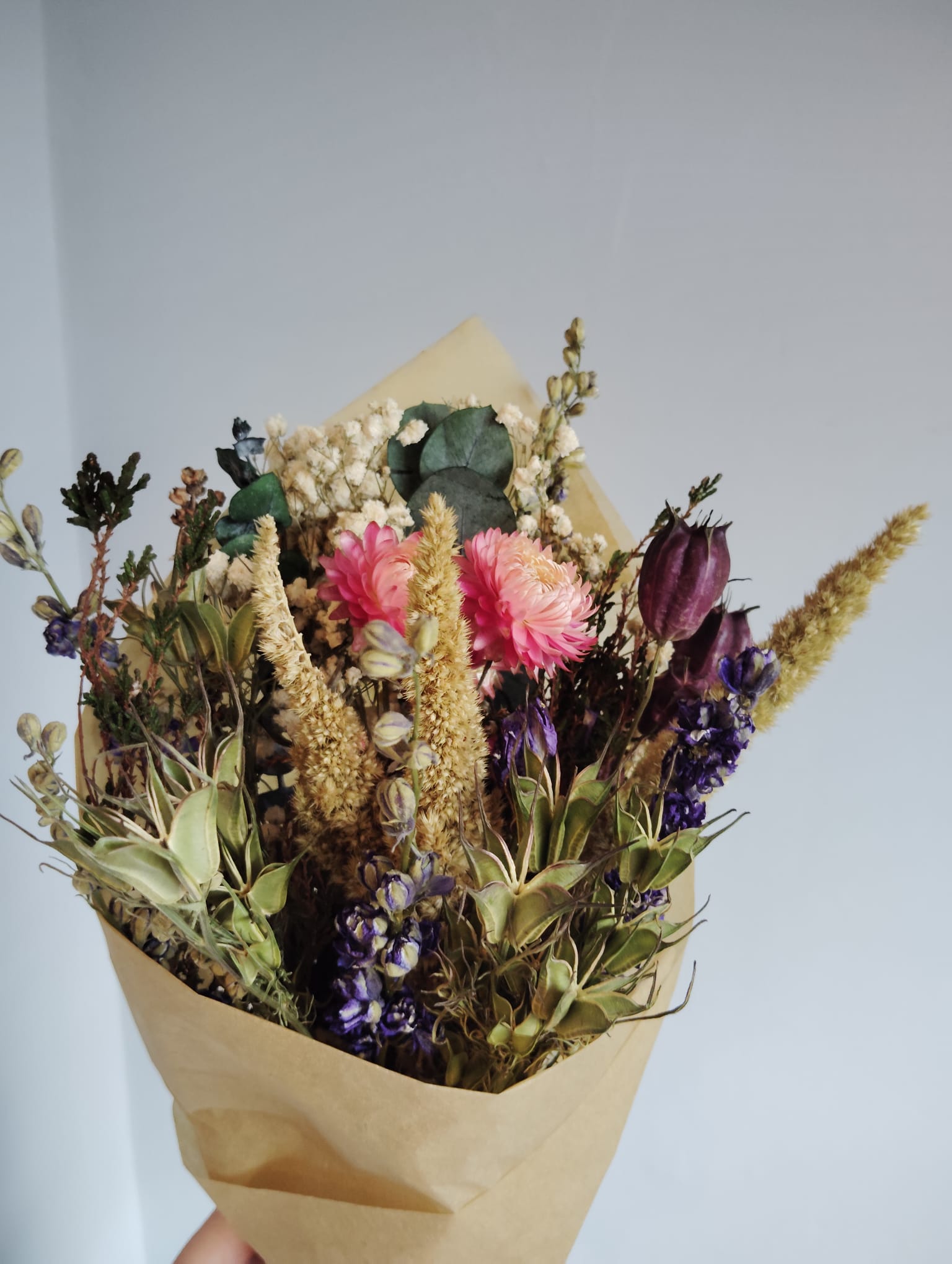 Hand-tied dried flower bouquet featuring pink strawflowers, purple larkspur, and natural grasses wrapped in eco-friendly kraft paper