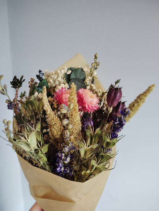 Hand-tied dried flower bouquet featuring pink strawflowers, purple larkspur, and natural grasses wrapped in eco-friendly kraft paper