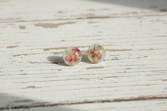 Light blue pressed flower circular stud earrings in clear resin on vintage dark blue book
