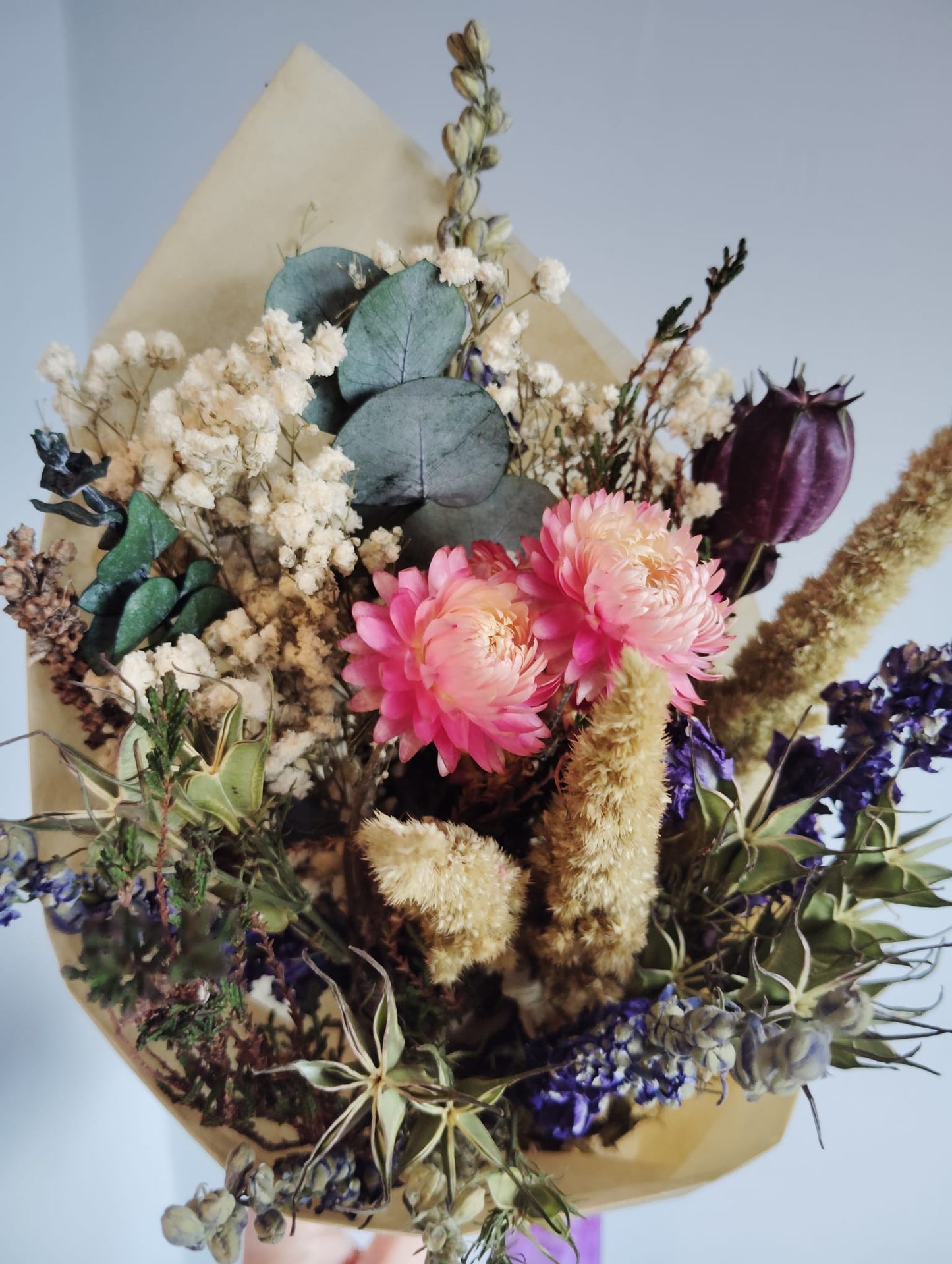 Close-up of a colorful dried flower wreath with yellow statice, red everlastings, and preserved eucalyptus leaves.
